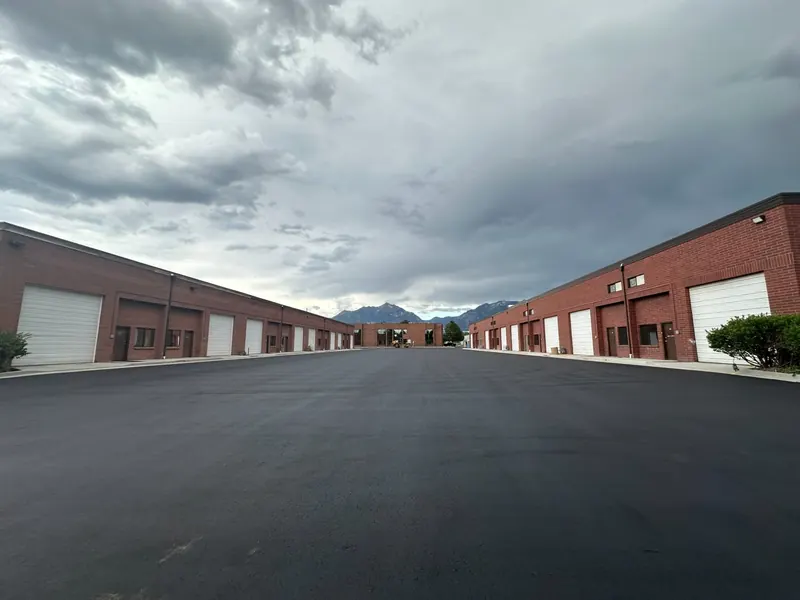 Two rows of brick industrial flex units with roll-up doors and the Wasatch mountains behind